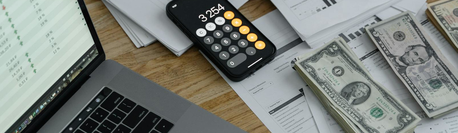A picture of a table with a smart phone, USD currency, and a laptop.