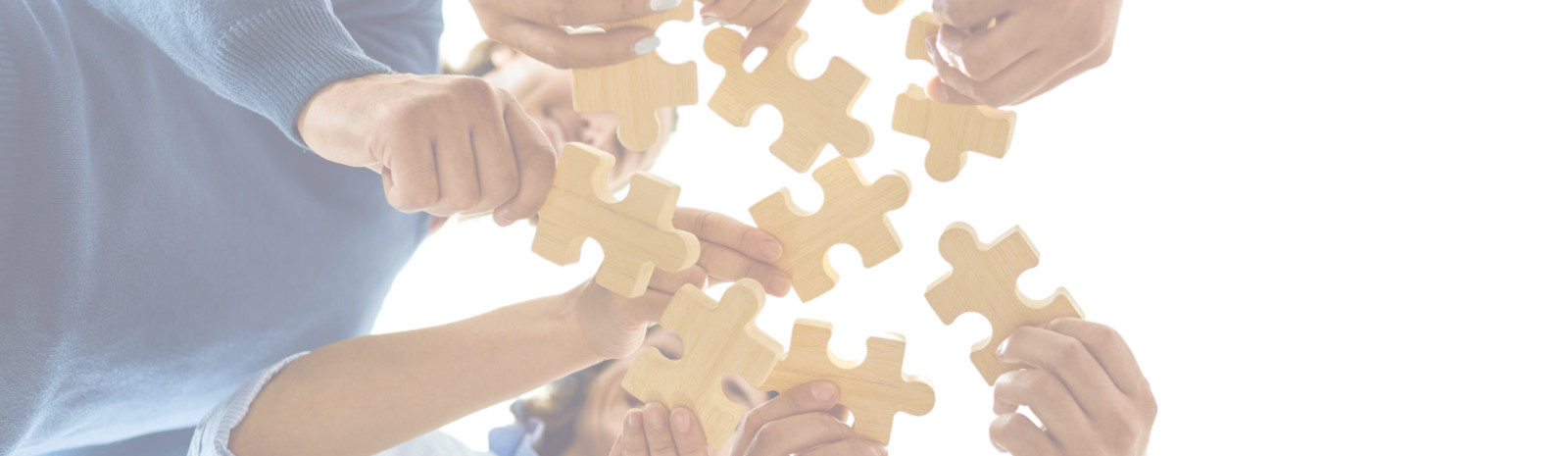 A picture of several people holding jigsaw puzzle pieces above a camera.