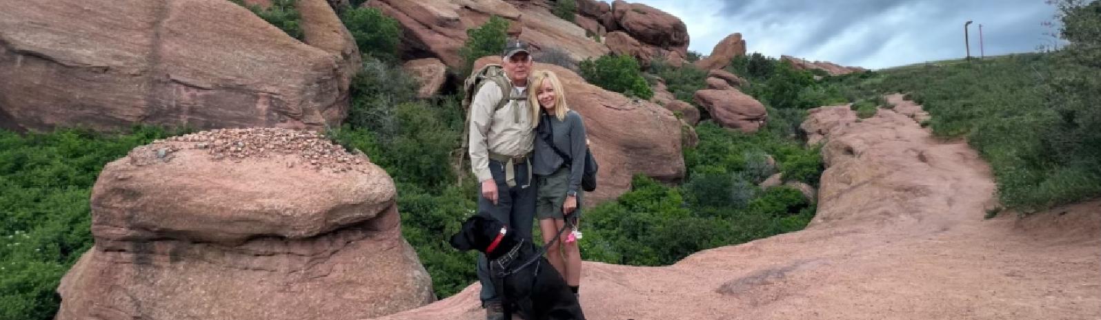 A picture of a couple standing on rocks with there dog.